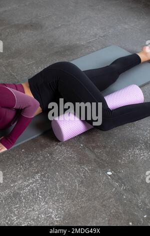 A young woman in sportswear performs a myofascial hip massage with a roller. Muscle recovery, mfr. Stock Photo