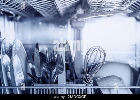 Front view of open automatic stainless steel built-in fully integrated top control dishwasher range machine with clean utensils, cutlery, glasses, dishes, plates inside in modern home kitchen Stock Photo