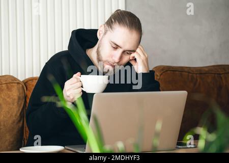Tired young man working on a laptop with a cup of coffee. Stock Photo