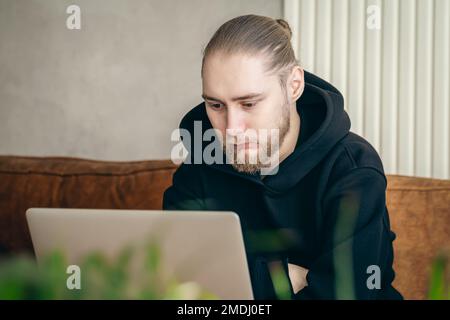 An attractive young man with a beard is working on a laptop. Stock Photo