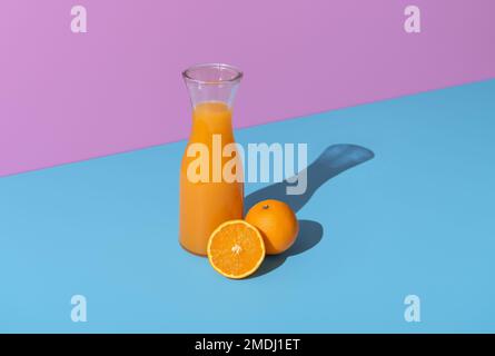Freshly squeezed orange juice in a glass carafe minimalist on a blue table. Oranges and orange juice in bright light on a vibrant colored background. Stock Photo