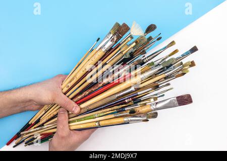 Paint brushes in male hands on a colored background, top view. Stock Photo