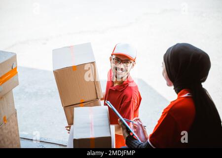 male worker smiling lifting box with female worker in hijab Stock Photo