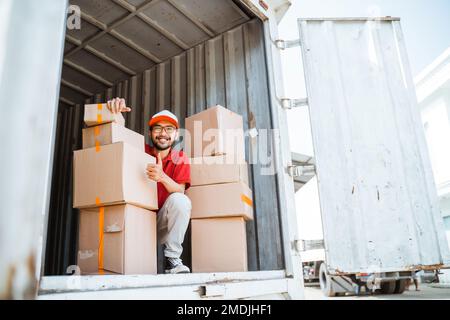 Smiling male employee with thumbs up while working unloading boxes Stock Photo