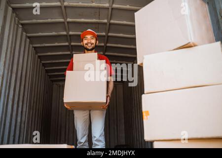 delivery man lifts out stacked cardboard boxes from container Stock Photo