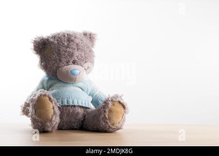 Gray teddy bear in light blue knitwear on white background. Stock Photo