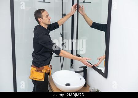 The worker installs the mirror in the bathroom. Stock Photo