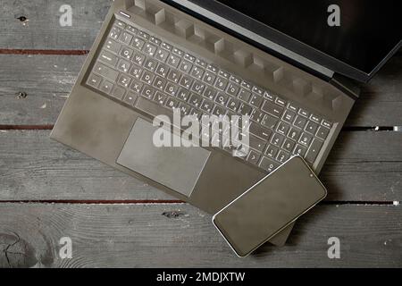 black laptop and phone lie on the written old wooden table, laptop on the table and phone Stock Photo