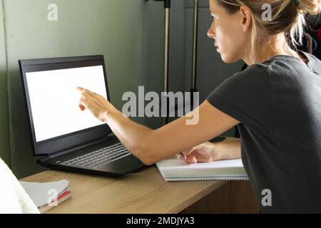 a girl sits at a table and looks at a laptop with a poor screen at home, working on self-isolation at home, a laptop with a poor screen Stock Photo