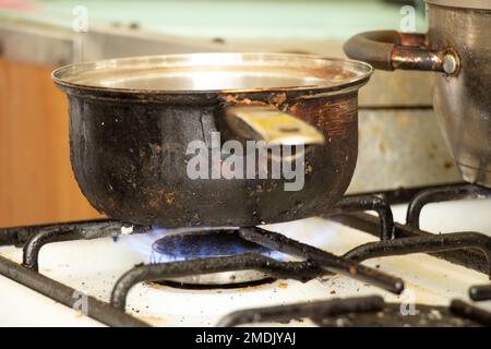 a dirty saucepan stands on a dirty gas stove in the kitchen at home, cooking soup on the stove, gas stove, kitchen Stock Photo