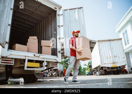 male worker in red uniform lifting package box from container Stock Photo