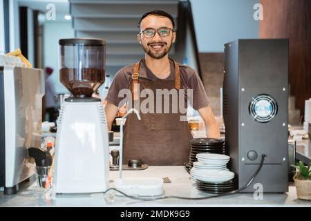 male barista smiling at camera standing behind barista counter Stock Photo