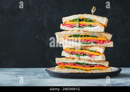 Big homemade sandwich with sausage, cheese and arugula on a dark concrete background Stock Photo