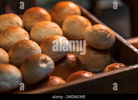 Close-up hot Fresh Baked Bread Rolls in a wooden box for the customer, the stack of freshly baked bread rolls, warm light from above. Stock Photo