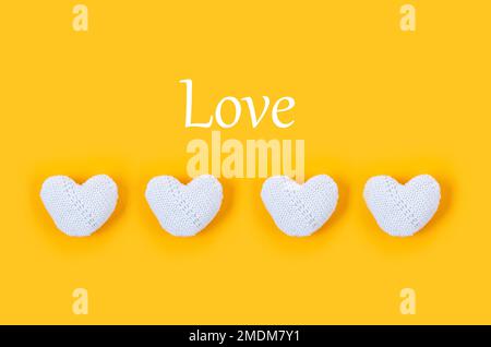 Many white knitted hearts with an inscription "love" on yellow background. Concept of Valentine day. Greeting card for Valentine,  Mother day or birth Stock Photo