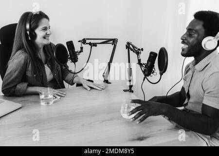 Multiracial hosts streaming podcast at digital studio - Main focus on left microphone - Black and white editing Stock Photo