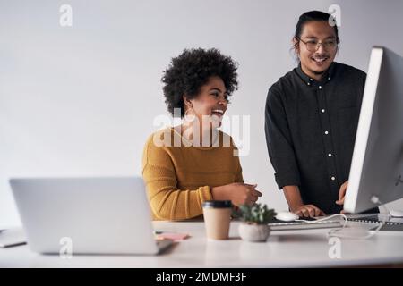 Laughter is essential for good teamwork. a two young coworkers working on a computer together in the office. Stock Photo