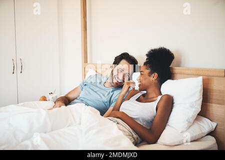 Just a chilled lovers morning. an affectionate young couple laughing together while lying in bed in the morning. Stock Photo