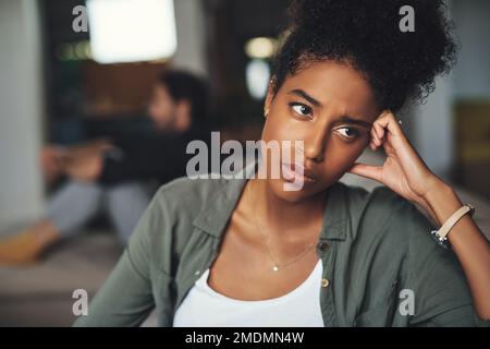 Nothing will ever be the same again. an attractive young woman looking upset while her boyfriend sits in the background at home. Stock Photo