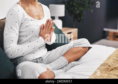 Spending time with yourself in the morning is essential. an unrecognizable woman sitting cross legged on the bed with her palms together in prayer at Stock Photo
