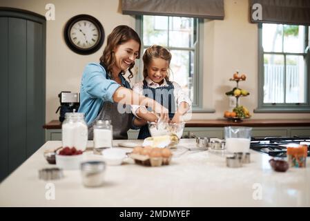 Baking keeps us happy and busy. a woman and her daughter baking together in the kitchen. Stock Photo