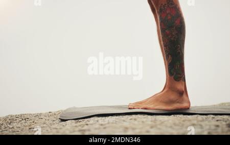 Be here now, be someplace else later. an unrecognizable person standing on a yoga mat while on the beach during an overcast day. Stock Photo
