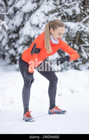 A female runner checks her sports performance using a smart watch. Running in winter and measuring heart rate. Stock Photo