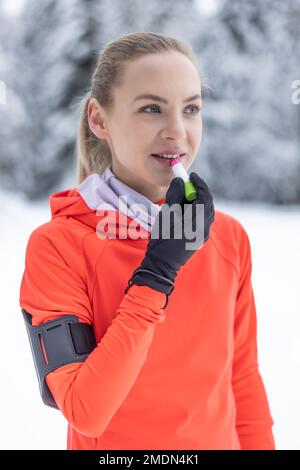 A young female runner applies protective balm to her lips due to the frosty weather, prevention of chapped and dry lips. Stock Photo