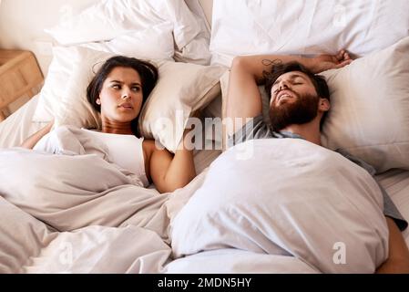 Wheres a mute button when you need one. a young woman covering her ears with a pillow while her husband snores in bed. Stock Photo