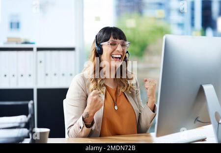 This is such a happy moment. an attractive young businesswoman celebrating while wearing a headset in her office during the day. Stock Photo