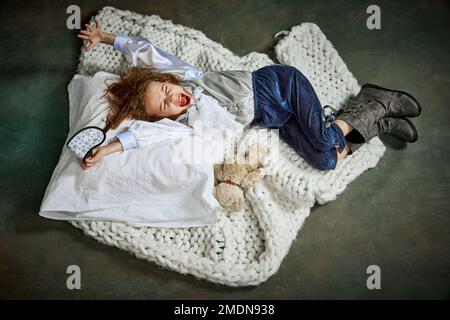 Happy morning, excited wake up. Ariel view of cute little girl in clothes sleeping on white blanket. Concept of napping day, dreams, happy childhood. Stock Photo