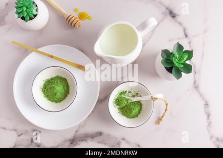 matcha tea powder in white ceramic bowls and a special bamboo measuring spoon on a marble table. top view. traditional Japanese tea Stock Photo