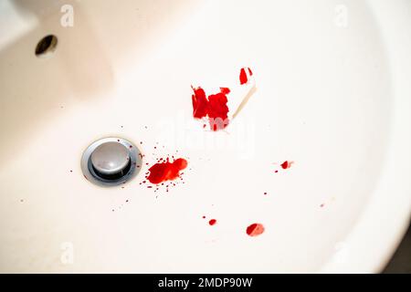 Red blood drops in white bathroom sink. Real blood as traces and evidence of a crime. Concept of nosebleed, injury, violence, murder or suicide. Blood Stock Photo