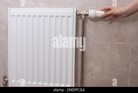 A woman regulates the gas heating in the room in order to save gas energy, taking into account the sanctions. Comfortable heating in the house. Stock Photo