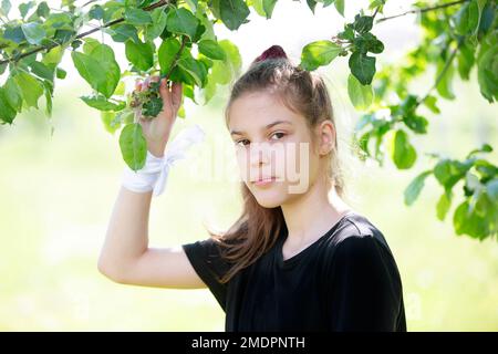 Portrait of a beautiful brown-eyed girl of ten years old against the background of green branches. Stock Photo