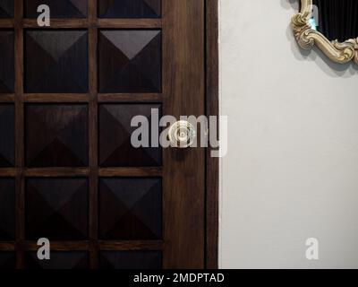 Old luxury brass door knob on vintage pattern wooden door with vintage mirror hanging on white wall background in the white room. Stock Photo