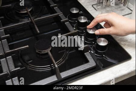 A woman turns on a gas stove with piezo ignition. Turns the gas regulator, danger Stock Photo