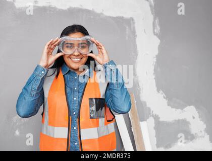 A female construction worker smiles and fits her safety goggles while on site Stock Photo