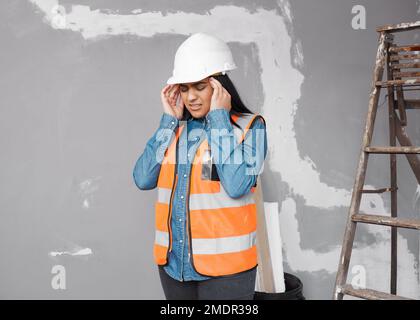 A young South Asian construction worker rubs her temples in pain, headache Stock Photo