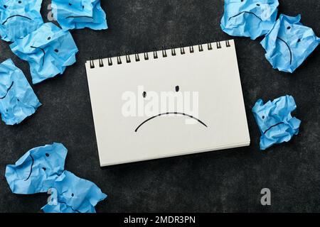 Blue crumpled sticky notes blank with drawing sad face on black background with copy space ready for your message. Blue Monday and mental health conce Stock Photo
