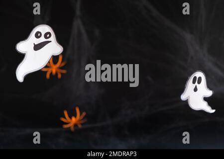 Two merry ghosts made of paper on a black background with spider webs and spiders. With space for text in the middle Stock Photo