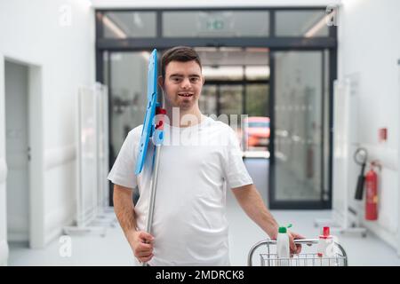 Young man with down syndrome working in a hospital as cleaner. Concpet of integration people with disability into society. Stock Photo