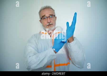 Portrait of doctor in protective coveral putting on surgical gloves. Stock Photo