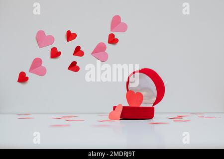 Paper hearts in two colors fly over the ring box in which a heart is placed. Decorative elements are isolated on a white background Stock Photo