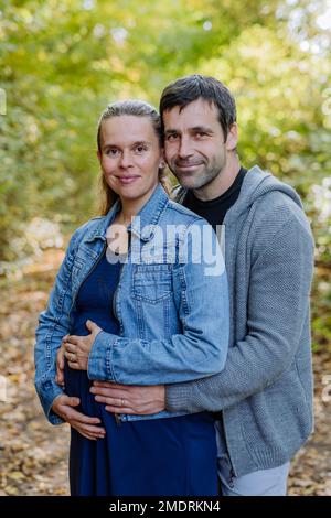 Portrait of happy pregnant woman and her husband, standing in forest. Stock Photo