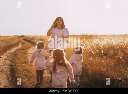 Mother and daughters triplets family time, blowing bubbles at sunset outdoors Stock Photo