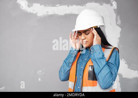 A young South Asian construction worker rubs her temples in pain, headache Stock Photo