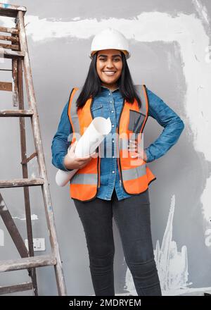 An attractive South Asian construction worker holds building plans under her arm Stock Photo