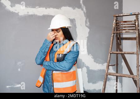 A young South Asian construction worker rubs her sinuses in pain, headache Stock Photo