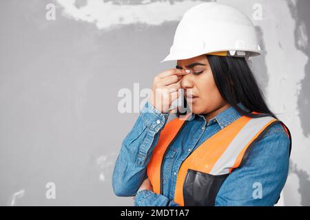 A young South Asian construction worker rubs her sinuses in pain, headache Stock Photo